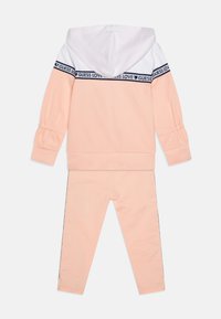 Peach-colored tracksuit set with a white hoodie, navy "GUESS LOVE" band, and elasticated sleeves; fitted leggings with side accents.