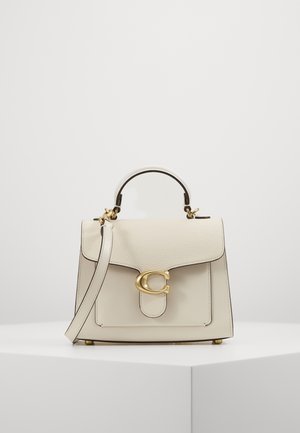 Sac à main en cuir crème avec poignée supérieure, fermoir doré en forme de lettre C et bandoulière assortie sur une surface et un fond blancs.