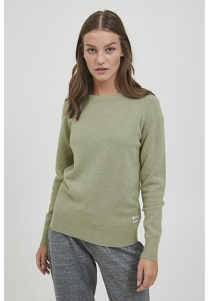 Light green sweater in soft fabric with a round neckline, ribbed cuffs, and hem; paired with gray sweatpants; minimal branding tag at hem.