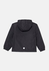Veste légère noire à capuche avec des poignets élastiques, présentant une texture lisse et un petit logo carré dans le bas du dos.