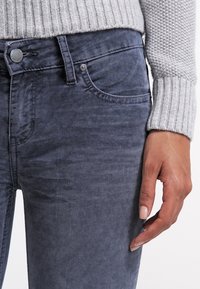 Mörkblå denimjeans med slim fit, med en klassisk femficksdesign och en subtil, strukturerad yta. Ljust grå ribbad tröja är synlig.