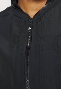 Black insulated jacket featuring a full zip front, high collar, patch pocket, and stitched detailing for added texture.