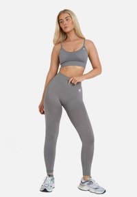 Completo sportivo grigio composto da un reggiseno sportivo a coste e leggings a vita alta con dettagli in rete. Include un branding minimale sul tessuto.