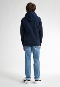 Sudadera azul marino con capucha ajustable, combinada con jeans de un azul claro. El conjunto presenta un corte relajado y un diseño minimalista.