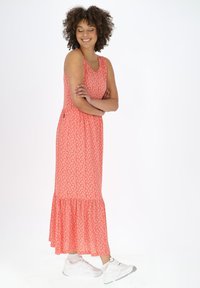 Maxikleid in Koralle mit weißem Blumenmuster, ausgestelltem Saum, ärmellosem Design und lockerer Passform, kombiniert mit weißen Sneakers.