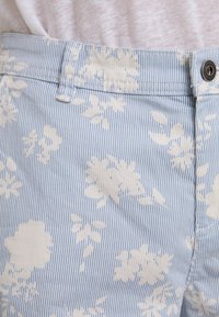 Lichtblauwe shorts met een bloemenpatroon in het wit, voorzien van dunne verticale strepen. Katoenen stof, eenvoudige tailleband en knoopsluiting.