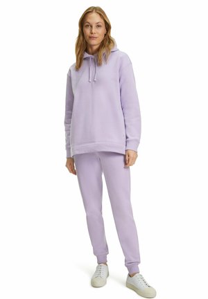 Haut à capuche lilas et pantalon de jogging assorti en tissu doux. Coupe ample avec une capuche à cordon de serrage et des pantalons à chevilles, accompagnés de baskets blanches.