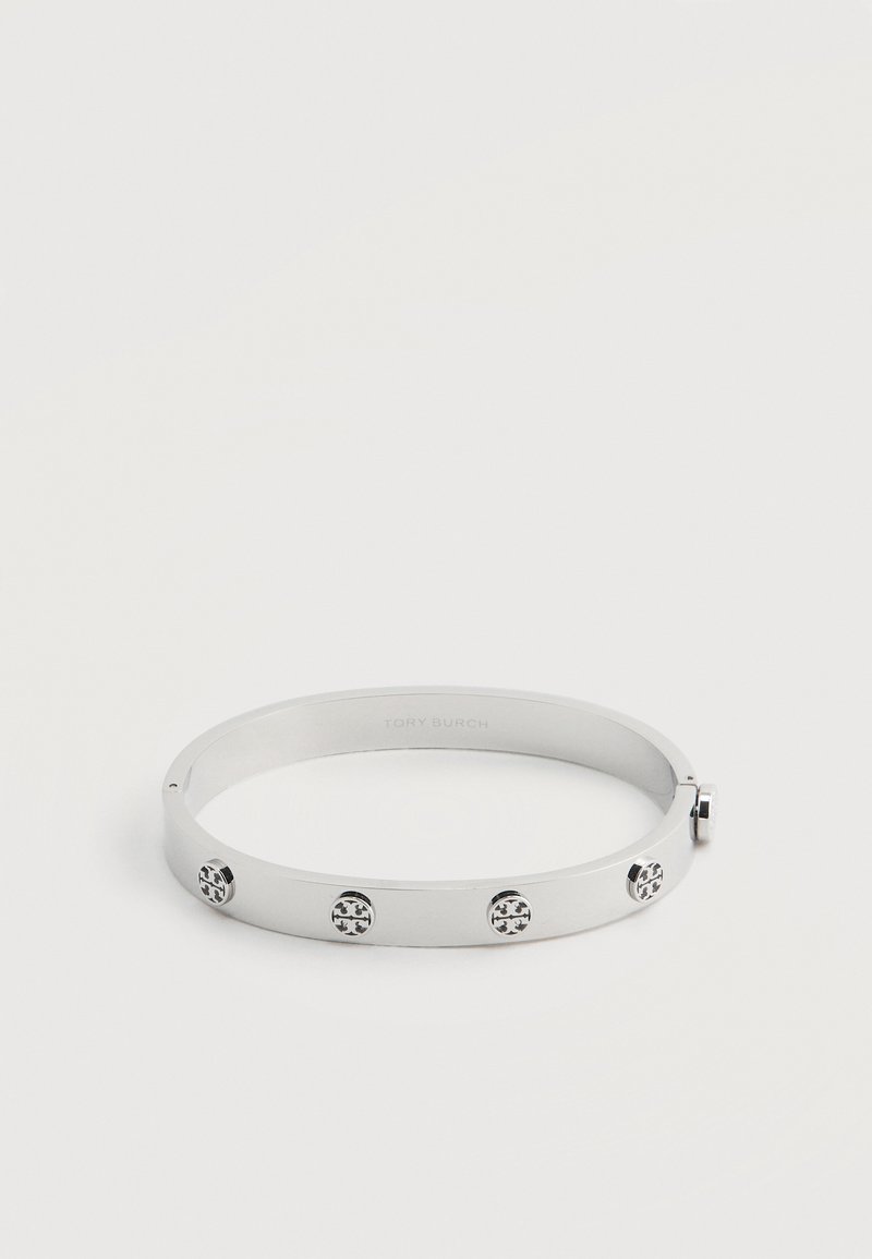 Βραχιόλι χειροπέδα από μέταλλο σε ασημί απόχρωση με τέσσερις στρογγυλές καρφίτσες λογότυπου, ισαπέχουσες, και κούμπωμα με αρθρωτό κλείστρο σε λευκό φόντο.