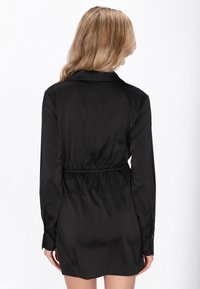 Černé saténové šaty s límečkem, dlouhými rukávy a elastickým pasem. Hladká textura s mírně lesklým povrchem.