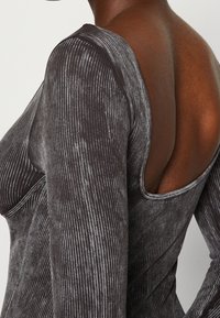 Body z długim rękawem w ciemnoszarym kolorze, z teksturowanej tkaniny w pionowe paski; posiada odkryty tył i dopasowaną sylwetkę.