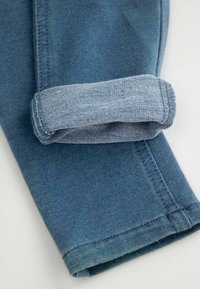 Niebieska nogawka dżinsowa z widocznym szwem, podwinięta przy mankiecie, aby odsłonić jaśniejszy kolor wewnętrznego materiału.