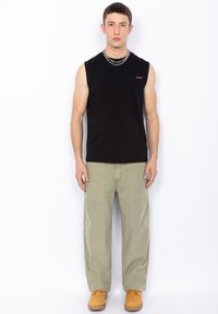 Top in cotone nero senza maniche con tasca frontale; pantaloni verde oliva a vestibilità ampia con tasche laterali; stivali marroni. Design semplice e funzionale.