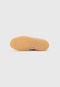 Sole of a sneaker with a textured rubber outsole in light brown, featuring circular and diamond patterns for grip.