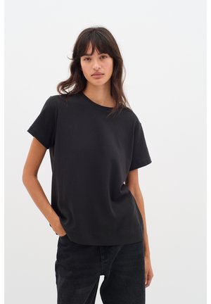 Sort bomulds-T-shirt med korte ærmer og rund halsudskæring. Enkel, afslappet pasform. Bær sammen med mørke denimjeans mod en lys baggrund.