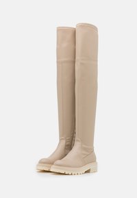 Beige knæhøje støvler lavet af syntetisk materiale med en glat tekstur, der har en kraftig hvid sål og syninger langs sømmene.