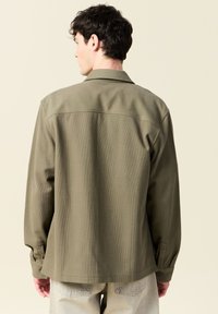 Olivgrön skjorta med texturerad tyg, skräddarsydd krage och knäppta manschetter, med en avslappnad passform och design med bakstycke.