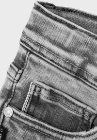 Jeans de mezclilla gris con un ligero desgaste, costuras visibles y un pequeño bolsillo frontal. Incluye un detalle de botón metálico.