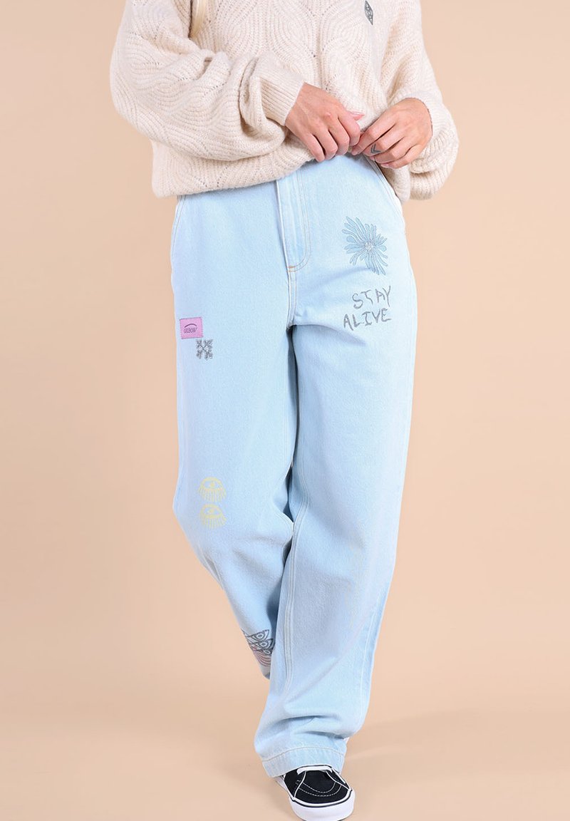 Jean en denim baggy bleu clair avec divers détails brodés, y compris des fleurs et des phrases, offrant une coupe décontractée et des chevilles retroussées.