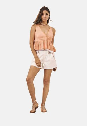 Top peplum color durazno con tirantes finos, cintura ceñida y tela recogida; combinado con pantalones cortos blancos con costuras decorativas.