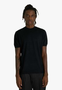 Maglione nero a maniche corte con scollo a girocollo in maglia, dalla trama liscia e silhouette aderente, abbinato a pantaloni scuri.