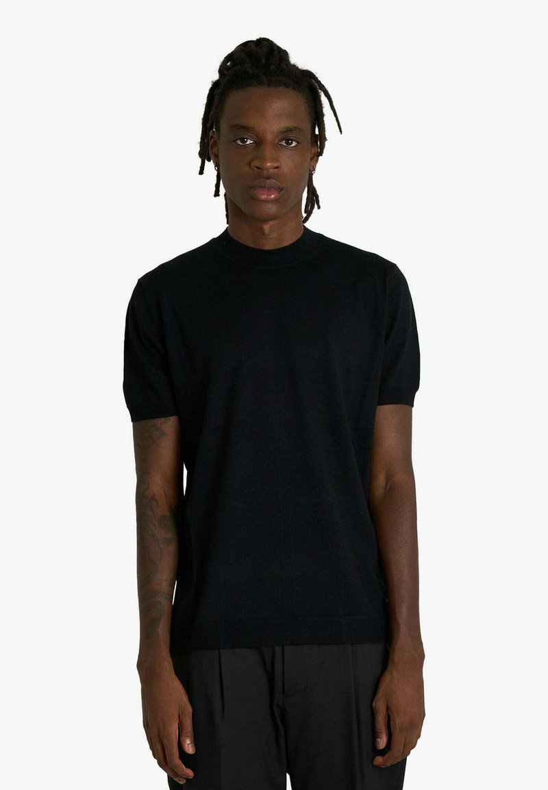 Maglione nero a maniche corte con scollo a girocollo in maglia, dalla trama liscia e silhouette aderente, abbinato a pantaloni scuri.