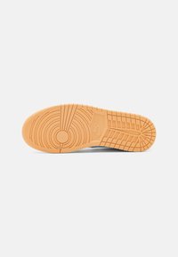 Nike sneaker sole in light orange rubber, featuring circular and horizontal tread patterns, with branding embossed on the heel area.