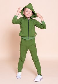 Zielona bluza z kapturem i dopasowane spodnie dresowe z miękkiego, elastycznego materiału. Posiadają zamek błyskawiczny, kieszenie oraz ściągacze.