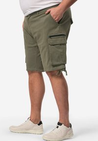 Pantaloni cargo verde oliva con multiple tasche, dettagli con cerniera e lacci regolabili all'orlo, realizzati in un tessuto robusto e testurizzato.