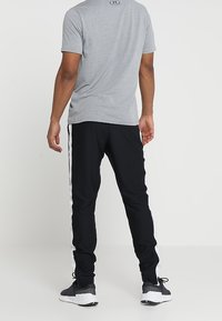 Graues T-Shirt mit kurzen Ärmeln und Rundhalsausschnitt, kombiniert mit schwarzen Jogginghosen mit weißen Seitenstreifen und elastischen Bündchen. Schwarze Sportschuhe.