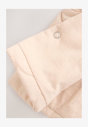 Hellbeige gesteppte Jacke mit glattem Stoff, versehen mit einem silbernen Druckknopfdetail und Steppnähten, die eine weiche, strukturierte Oberfläche zeigen.