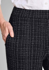 Pantaloni neri a motivi realizzati in tessuto testurizzato, dotati di una ampia fascia elastica in vita e tasca laterale con un sottile design lineare bianco.
