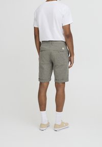 Shorts gris à carreaux avec des ourlets retournés, deux poches arrière avec des boutons et une étiquette de logo. Associés à un t-shirt blanc uni et des chaussures légères.
