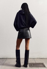Schwarzer oversized Hoodie, Leder-Minikleid und kniehohe schwarze Stiefel. Weicher Stoff mit lockerer Passform, der die Beine und die Silhouette betont.