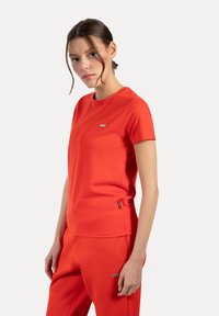 Camiseta roja ajustada hecha de un tejido suave, con mangas cortas, un cuello redondo y un pequeño detalle de logo en el pecho y el dobladillo.