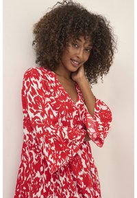 Rote und weiße Blume gemusterte Kleid mit tiefem V-Ausschnitt und weit ausgestellten Ärmeln. Hergestellt aus leichtem Stoff mit plissierter Textur.