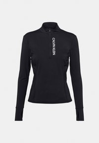 Černý sportovní top s dlouhým rukávem a čtvrtinovým zipem, s otvory na palce, který má na hrudi vertikální bílý text "CALVIN KLEIN".