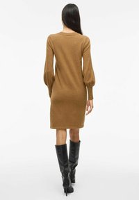 Brown knitted dress with long, puffed sleeves, a fitted silhouette, and a round neckline. Worn with high black leather boots.