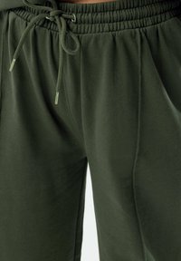 Mörkgr öna, mjuka joggers i tyg med elastisk midja och justerbar dragsko. Har sidofickor och en avslappnad passform.