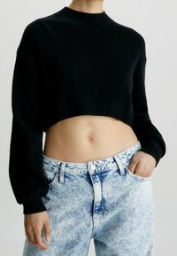 Schwarzer, kurzer Pullover mit gerippter Textur und rundem Ausschnitt, kombiniert mit hochtaillierten, hellblauen, ausgeblichenen Jeans.
