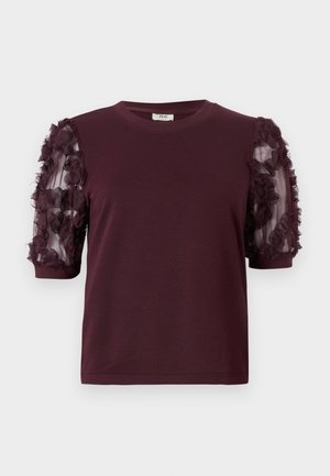 Burgundi színű, rövid ujjú póló, puha anyagból készült, tüll ujjak díszítik, amelyek textúrált virágos fodrokkal vannak ékesítve.