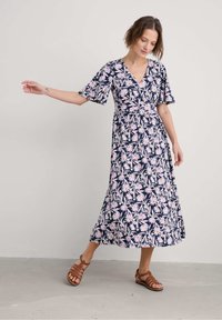 Floral midi dress in navy blue with light pink and white flowers. Short, wavy sleeves and a fitted waist with a flared skirt. Brown strappy sandals.