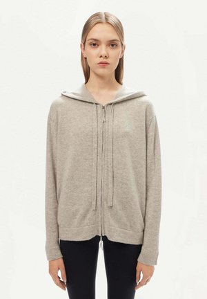 Sweat à capuche zippé gris clair en tissu doux, avec capuche à cordon, manches longues et coupe décontractée. Ourlets et poignets accentués.