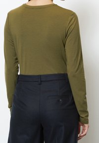 Olivgrön långärmad skjorta kombinerad med mörkblå byxor som har en bakficka med knapprad. Slät textur, figursydd design.