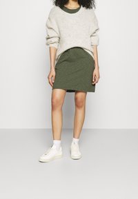 Un pull en tricot surdimensionné gris clair, une robe verte olive et des baskets blanches à semelles texturées ; couches subtiles, coupe décontractée et design sportif.