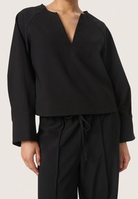 Svart kort topp med V-ringning, breda ärmar och ribbad textur, kombinerad med matchande högmidjade byxor. Har justerbar dragsko.