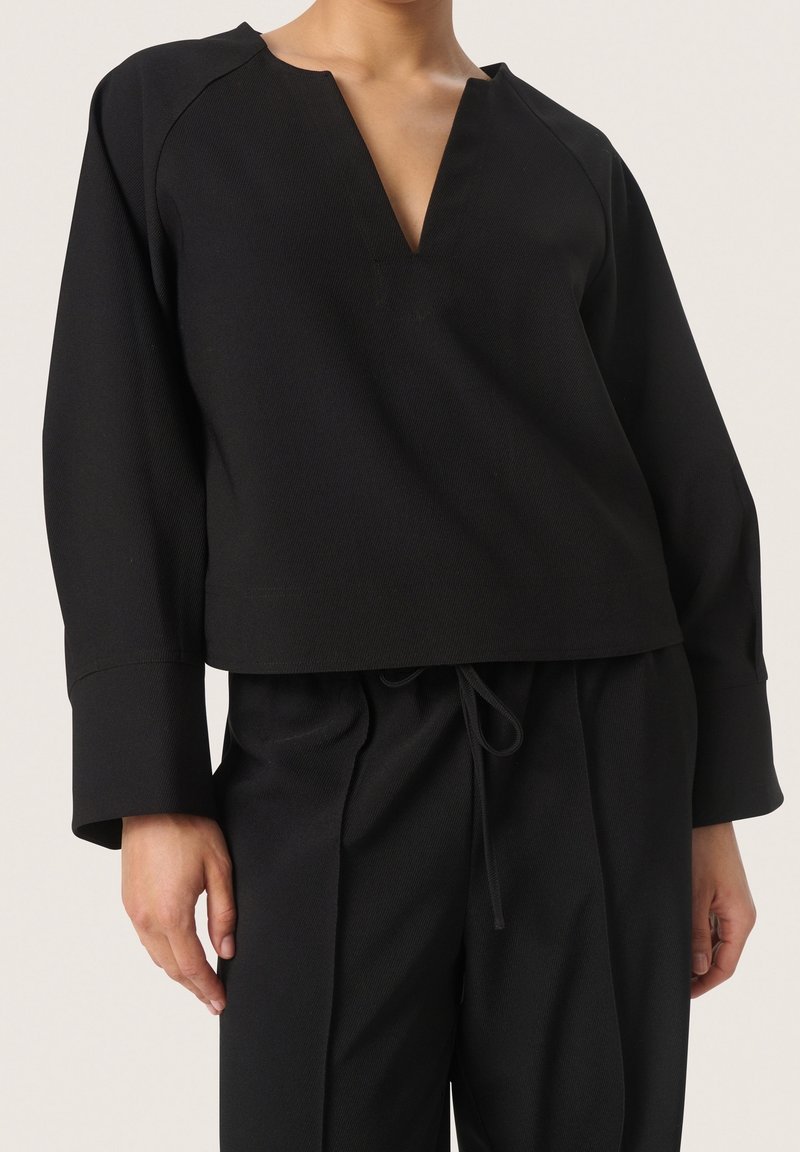 Svart kort topp med V-ringning, breda ärmar och ribbad textur, kombinerad med matchande högmidjade byxor. Har justerbar dragsko.