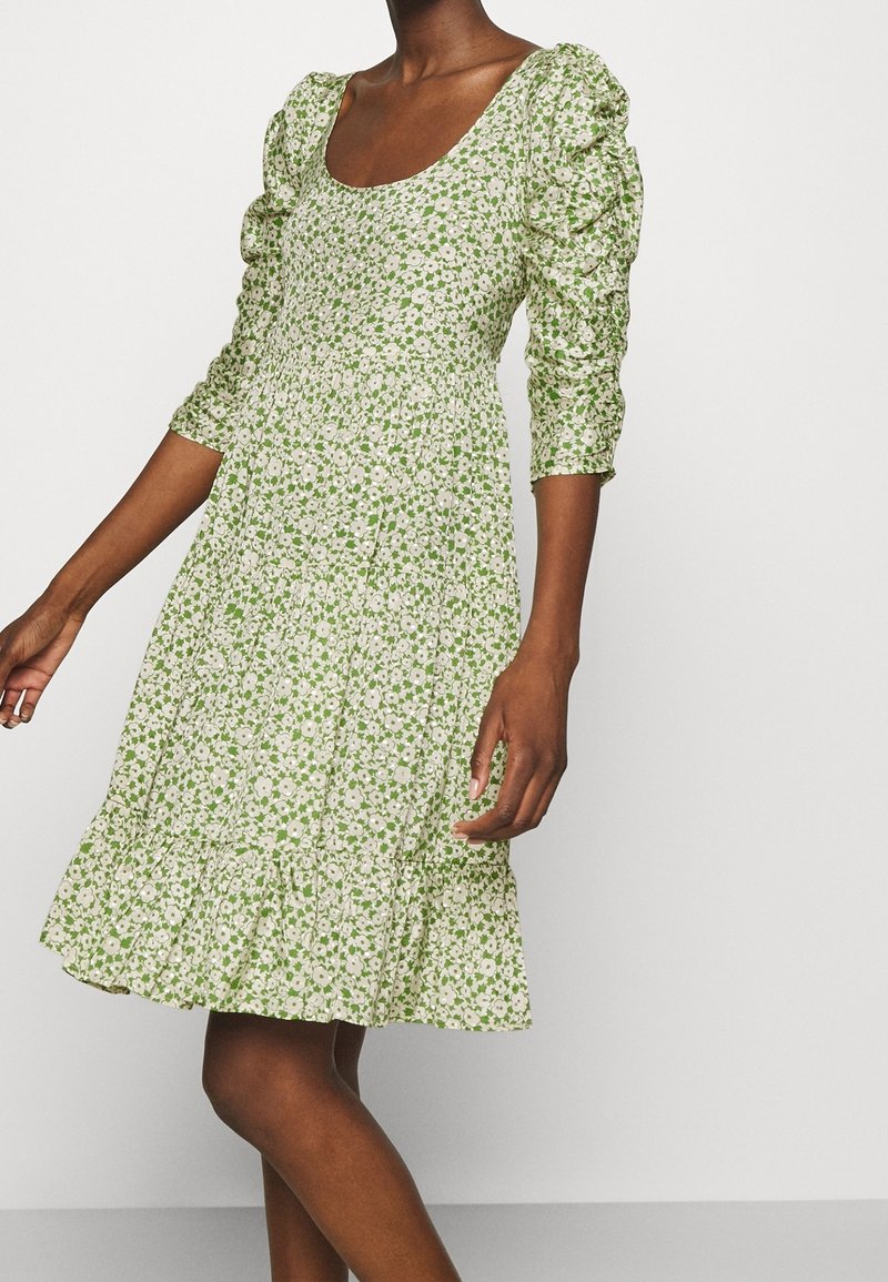 Floral dress with a green base and white flowers, featuring puffed sleeves and a ruffled hemline, made of lightweight fabric.