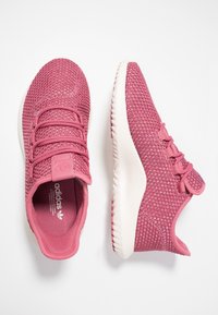 Rosa atletiska skor med en texturerad mesh-overdel, elastiska snörningar och en dämpad sula. Har en logotyppatch på tungan och en rund tå.