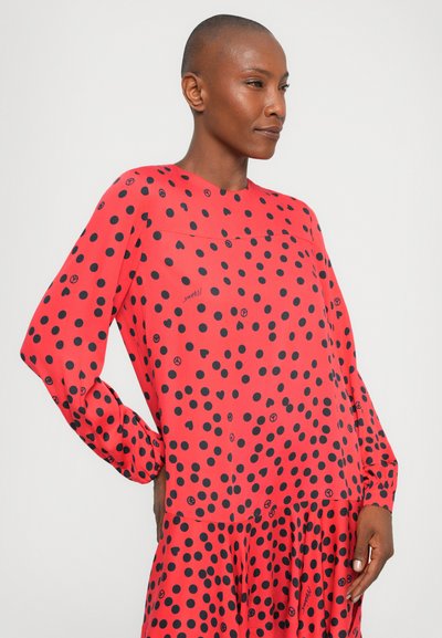 Rochie roșie cu un model în buline negre. Mâneci lungi, croi lejer, decolteu rotund și detaliu cu fustă plisată.