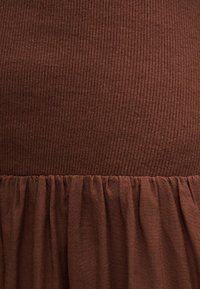Robe marron présentant une texture côtelée sur le haut et une jupe fluide froncée. Le matériau semble doux et léger.